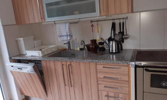 A modern kitchen with wood fronts and a granite countertop. The dishwasher is open and there are various kitchen appliances on the wall.