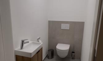 A modern bathroom with a white toilet and a sink. The walls are styled in light colors and the floor is gray tiled.