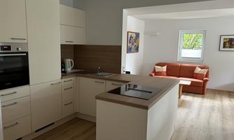 A modern kitchen with bright cabinets and a wooden countertop. In the background, there is a cozy living room with a red sofa.