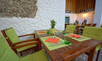 A cozy restaurant with wooden tables and green chairs. In the background, guests are sitting and enjoying their meal.