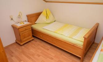 A simple bedroom with a single bed and a nightstand. On the bed are yellow and white bed linens.