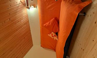 A cozy living room with an orange sofa and cushions. The ceiling is made of wood and there is soft lighting on the wall.