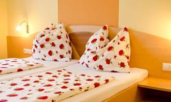 A cozy bedroom with a double bed and pillows with a rose pattern. The walls are in soft colors and the lighting is warm.