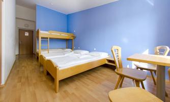 A simple room with two beds and a table. The walls are painted in a light blue and the floor is made of wood.
