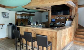 A cozy bar with a wooden counter and chairs. The rooms are designed to be bright and inviting.
