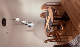 A modernly furnished dining area with a round wooden table and four chairs. Three stylish lamps hang above the table, providing pleasant light.