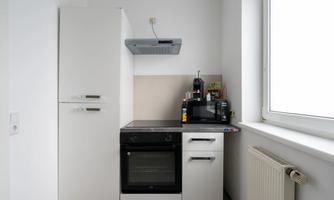 A modern kitchen with a refrigerator, a stove, and a graphics card setup. It has bright walls and a large window area.