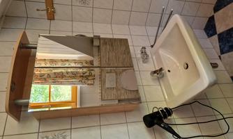 A bathroom with a sink and a large mirror. A hairdryer is hanging on the wall and there is a window with curtains.