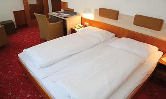 A bright room with a double bed and white bedding. The decor is simple and modern, with red carpeting.