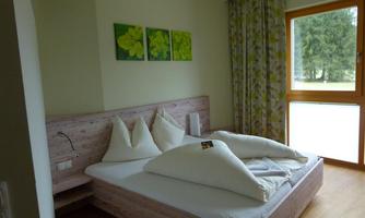 A cozy bedroom with a large bed and bright pillows. The walls are painted in soft tones, and the room has a window with a view of the greenery.