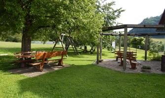 A beautiful garden with green grass and shade-giving trees. There are wooden benches and a swing for children.
