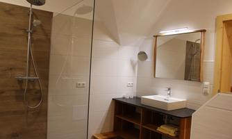 A modern bathroom with a glass shower and a stylish sink. There is a large mirror and wooden shelves for towels.
