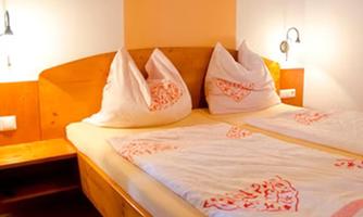 A cozy bedroom with a double bed and two large pillows. The walls are painted in gentle colors and there is a small nightstand.