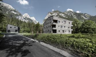 A modern architecture amidst mountains and green nature. In the foreground is a road that leads to the buildings.