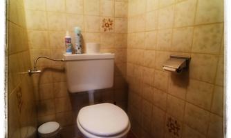 A small bathroom with a toilet and a toilet paper holder. On the wall hangs a sticker with the name "PAULA".