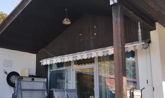 A cozy house with a porch and a table with chairs. Next to the house, there is a shelf and a wall with protective devices.