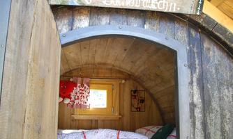A cozy sleeping area in a wooden house. Two beds with red and white blankets are visible.