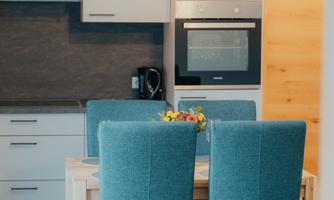 A modern kitchen with blue dining chairs and a wooden table. The walls are light and there is an inviting atmosphere.