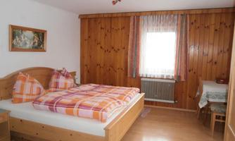 A cozy bedroom with a large wooden bed and warm wooden decor. The colorful cushions and window decoration give the room an inviting atmosphere.