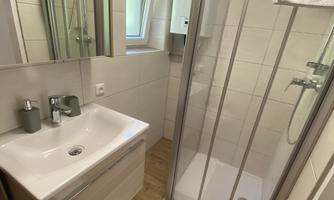 A modern bathroom with a shower, a sink, and mirrors. The floor is made of wood and the walls are brightly tiled.