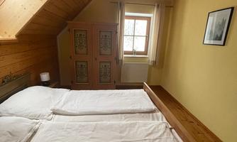 A cozy bedroom with a sloping ceiling and wooden panels. There are two beds, a window with a view outside, and yellow wallpaper.
