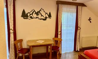 A cozy room with a wooden table and two chairs. On the wall, there is a mountain motif as well as curtains in red and white.