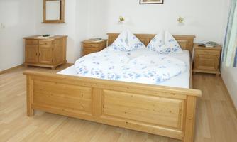 A simple bedroom with a large wooden bed and two pillows. There are also wooden furniture and a bright, cheerful floor.
