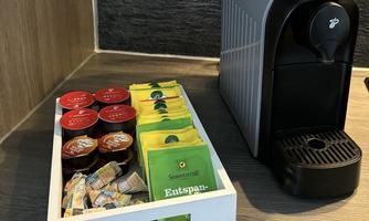 An elegant coffee station with a coffee machine, a selection of coffee capsules, and various tea bags. Additionally, small cream portions are placed in a white box.
