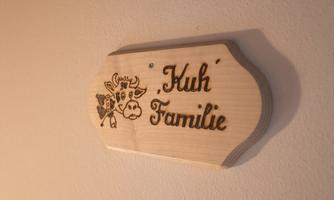 A wooden nameplate with the inscription "Cow Family" and a calf drawing. It is mounted on a wall and has a rustic design.