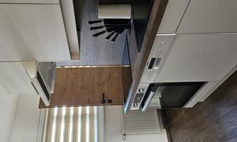 A modern kitchen with white cabinets and wood details. The equipment includes a stove, a sink, and an elegant countertop.