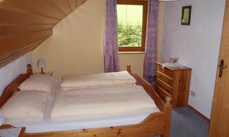 A cozy bedroom with a double bed and wooden furniture. The room has windows with curtains and offers a view of the greenery.