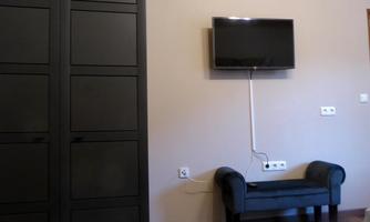 A modern room with a black wardrobe and a television on the wall. A small seating area with a dark bench completes the decor.