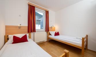 A simple room with two single beds and red cushions. A window lets in natural light and offers a view outside.