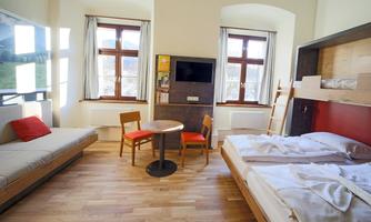 A bright room with two beds and a cozy sofa. There is a table with two chairs and large windows that let in plenty of light.