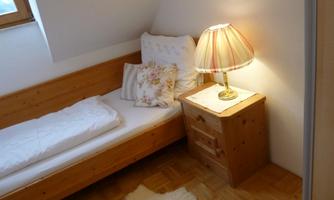A cozy bedroom with a single bed and a nightstand. A lamp provides warm light and a friendly atmosphere.