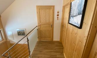A bright hallway with wooden decor and a metal handrail. A picture hangs on the wall, and to the right, a closed door is visible.