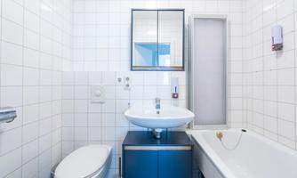 A modern bathroom with white tiles. It is equipped with a sink, a bathtub, and a toilet.