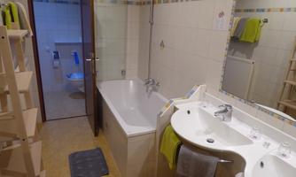 A modern bathroom with a bathtub and a double sink. The walls are tiled in light color, and there are towels in green color.
