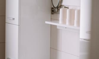 A modern bathroom with a white sink and a large mirror. There is a towel rack and several toiletries on a shelf.
