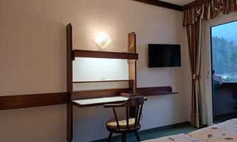 A cozy hotel room with a desk and a television.  
Windows overlooking the outside and a hint of nature.