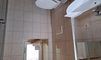 A bright bathroom with a modern toilet and a sink. The room is equipped with white tiles and a window.