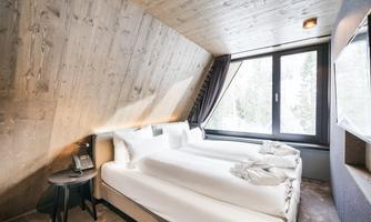 A modern room with three beds and wood paneling. Large windows offer views of the surrounding nature.