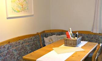 A cozy dining area with a wooden tray and a bench. On the table, there is a basket with kitchen utensils.