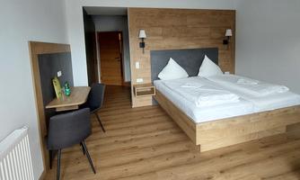 A modern hotel room with a double bed and a wooden background. There is a small desk and chairs, as well as a warm wooden floor.