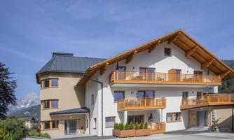 A modern house with wooden cladding and several balconies. The surroundings are mountainous and offer a clear view.