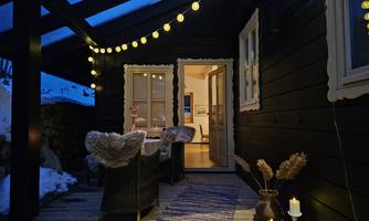 A cozy porch with warm light and stylish furniture. In the background, the entrance to a popular living space is visible.