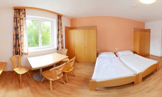 A bright room with two beds, a table, and chairs. The walls are painted in soft colors and the window offers a view of greenery.