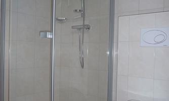 A modern bathroom with a glass shower and a toilet. The walls are light and the tiles are in neutral colors.