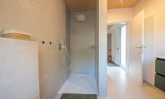 A modern shower with simple concrete walls and a bright, minimalist design. The space is well-lit and open.