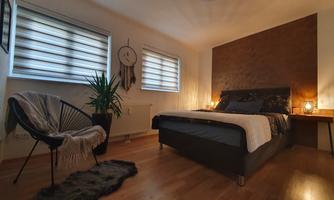 A modern bedroom with a cozy bed and stylish decor. A corner with an armchair and plants creates a relaxed atmosphere.